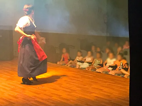 Bailaora con mantón sobre el escenario ante un público infantil sentado en el suelo