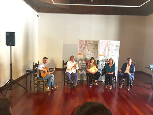 Guitarrista y ponentes durante una charla en una sala con público sentado
