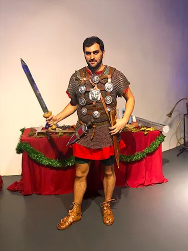 Recreador vestido de legionario romano con espada y coraza junto a una mesa