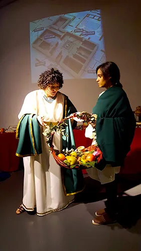 Dos mujeres con túnica romana y una cesta de frutas ante una proyección